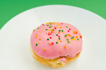 Pink round donut on white plate on green background