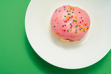 Pink round donut on white plate on green background