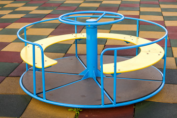 Playground in kindergarten with soft flooring and colorful bright merry-go-round outdoors.