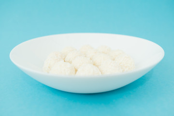 Chocolate covered coconut candies on white plate isolated on blue background. Truffle candy set. Selective focus