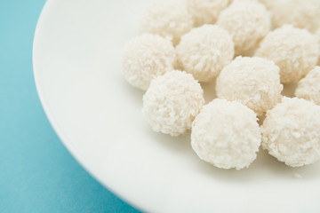 Chocolate covered coconut candies on white plate isolated on blue background. Truffle candy set. Selective focus