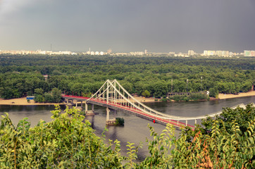View of pedestrian Park bridge over the Dnipro river. Cloudy sky after rain. Summertime