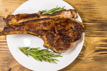 Roasted beef rib eye steak on bone with rosemary in white plate on wooden table