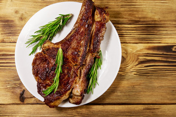 Roasted beef rib eye steak on bone with rosemary in white plate on wooden table