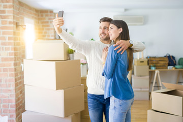 Beautiful couple taking a selfie photo using smartphone at new apartment, smiling happy for new house