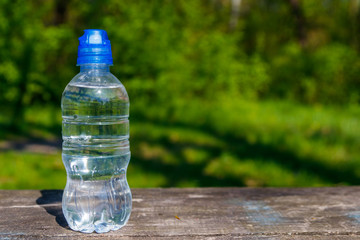 Plastic bottle with fresh drinking water on a wooden table on nature background