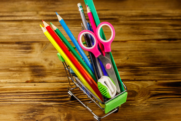 Buying school supplies. Shopping cart with school supplies on a wooden background. Back to school concept