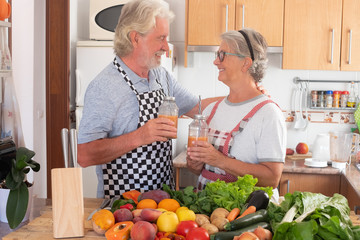 Happy couple of senior people enjoying the juice fruit just made. Looking each other with tenderness. Wooden table with a large group of colorful fruits and vegetables. Healthy eating