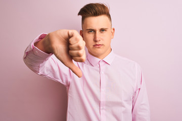 Young handsome businessman wearing elegant shirt standing over isolated pink background looking unhappy and angry showing rejection and negative with thumbs down gesture. Bad expression.