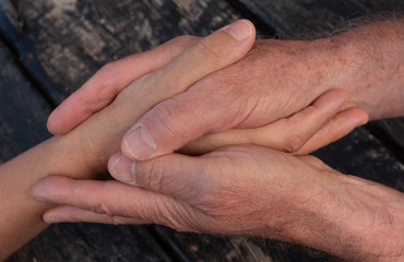 Take care of loved ones. Two hands of an elderly man shaking another person's hand. To convey trust, support and friendship. Wooden black table
