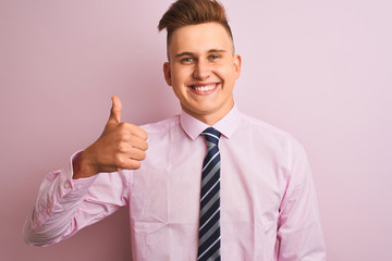 Young handsome businessman wearing shirt and tie standing over isolated pink background doing happy thumbs up gesture with hand. Approving expression looking at the camera showing success.