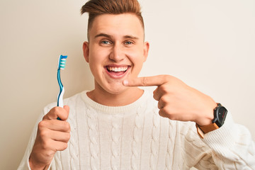 Young handsome man holding tooth brush standing over isolated white background very happy pointing with hand and finger