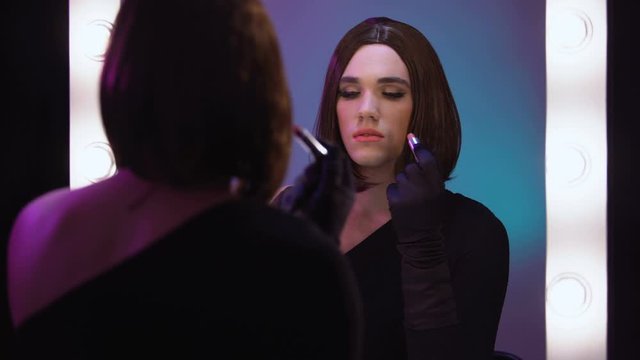 Attractive travesty celebrity applying lipstick looking in mirror, beauty care