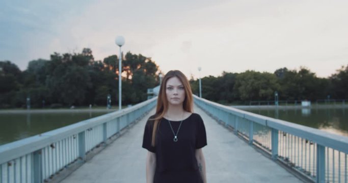 Young woman with nose piercing dressed in black walks toward the camera on a bridge in slow motion