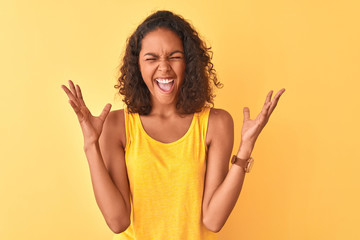 Young brazilian woman wearing t-shirt standing over isolated yellow background celebrating mad and...