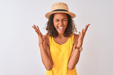 Obraz na płótnie Canvas Young brazilian woman wearing yellow t-shirt and summer hat over isolated white background celebrating mad and crazy for success with arms raised and closed eyes screaming excited. Winner concept