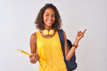 Brazilian student woman wearing backpack holding notebook over isolated white background very happy pointing with hand and finger to the side - obrazy, fototapety, plakaty