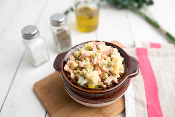 Bowl of traditional Russian salad called Olivie, Russian New Year or Christmas salad on wooden background. Salad from cooked vegetables. Potato salad. 