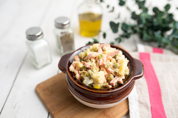 Bowl of traditional Russian salad called Olivie, Russian New Year or Christmas salad on wooden background. Salad from cooked vegetables. Potato salad. 