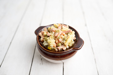 Bowl of traditional Russian salad called Olivie, Russian New Year or Christmas salad on wooden background. Salad from cooked vegetables. Potato salad. 