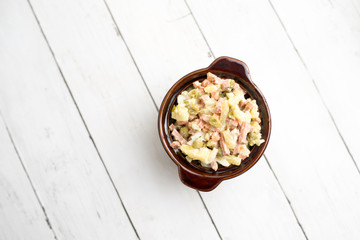 Bowl of traditional Russian salad called Olivie, Russian New Year or Christmas salad on wooden background. Salad from cooked vegetables. Potato salad. 