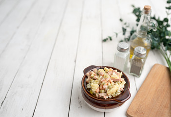 Bowl of traditional Russian salad called Olivie, Russian New Year or Christmas salad on wooden background. Salad from cooked vegetables. Potato salad. 