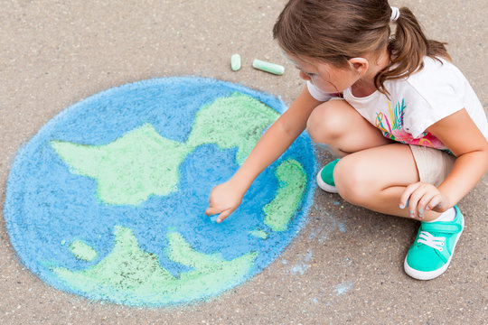 the  child girl draws a planet of the world with colored chalk on the asphalt. Children's drawings, paintings and concepts. Education and art, be creative when you return to school.  earth, Peace day