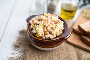 Bowl of traditional Russian salad called Olivie, Russian New Year or Christmas salad on wooden background. Salad from cooked vegetables. Potato salad. 