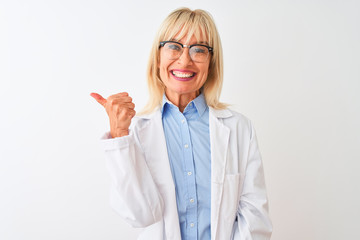 Middle age scientist woman wearing glasses standing over isolated white background smiling with happy face looking and pointing to the side with thumb up.