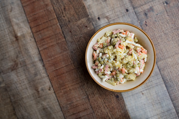Bowl of traditional Russian salad called Olivie, Russian New Year or Christmas salad on wooden background. Salad from cooked vegetables. Potato salad. 