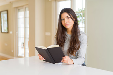 Young woman reading a book with a confident expression on smart face thinking serious