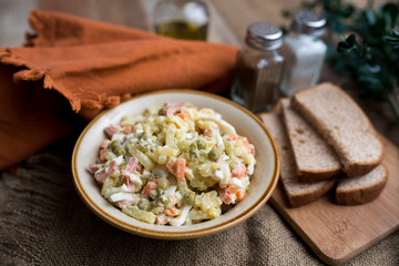 Bowl of traditional Russian salad called Olivie, Russian New Year or Christmas salad on wooden background. Salad from cooked vegetables. Potato salad. 
