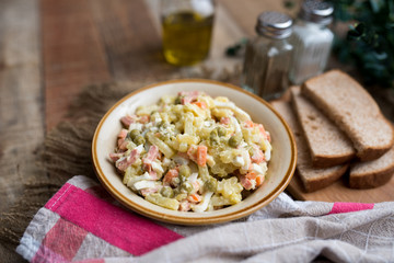 Bowl of traditional Russian salad called Olivie, Russian New Year or Christmas salad on wooden background. Salad from cooked vegetables. Potato salad. 