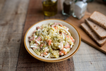 Bowl of traditional Russian salad called Olivie, Russian New Year or Christmas salad on wooden background. Salad from cooked vegetables. Potato salad. 