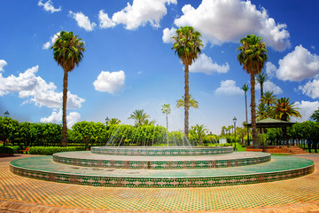 Fountain near Koutoubia Mosque minaret at medina quarter of Marrakesh, Morocco. There is beautiful green garden with palms. Blue sky is in the background.