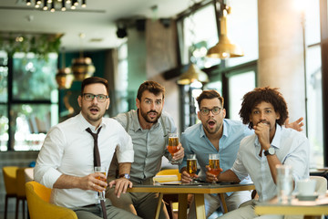 Four male friends are watching game drinking beer at the pub.