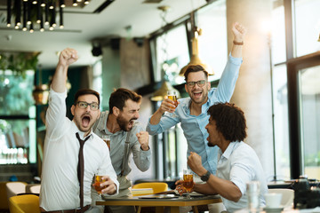 Four male friends are watching game drinking beer at the pub.