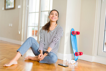 Young woman sitting on the floor using skateboard and headphones looking away to side with smile on face, natural expression. Laughing confident.