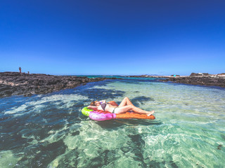 Girl sunbathing on an inflatable mattress shaped like ice cream cone floating on tropical water. Beautiful woman lying on a mat relaxing during exotic heavenly vacation. Holiday relax travel concept