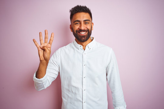 Young indian businessman wearing elegant shirt standing over isolated pink background showing and pointing up with fingers number four while smiling confident and happy.
