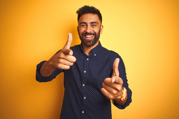 Young handsome indian businessman wearing shirt over isolated yellow background pointing fingers to camera with happy and funny face. Good energy and vibes.