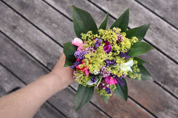 Fototapeta na wymiar Hand holding a bouquet (Sweet Pea, Oregano, Lavender, Dew cap) picked in the garden during Summer.