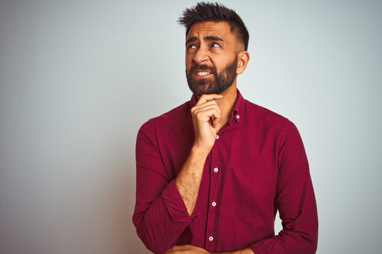 Young indian man wearing red elegant shirt standing over isolated grey background Thinking worried about a question, concerned and nervous with hand on chin