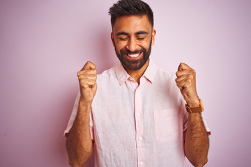 Young indian man wearing casual shirt standing over isolated pink background excited for success with arms raised and eyes closed celebrating victory smiling. Winner concept.