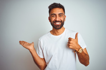 Young indian man wearing t-shirt standing over isolated white background Showing palm hand and...