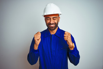 Handsome indian worker man wearing uniform and helmet over isolated white background excited for...