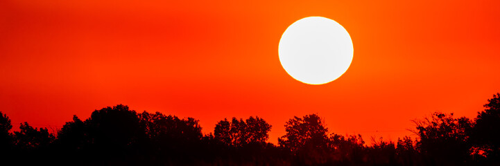 Bright sun in an orange sky with clouds at sunset