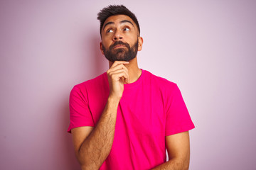 Obraz premium Young indian man wearing t-shirt standing over isolated pink background with hand on chin thinking about question, pensive expression. Smiling with thoughtful face. Doubt concept.