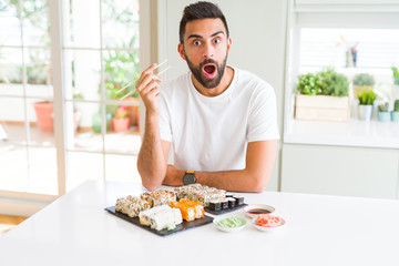 Handsome hispanic man eating asian sushi using chopsticks scared in shock with a surprise face, afraid and excited with fear expression