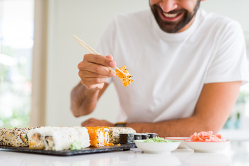 Handsome man smiling happy enjoying eating fresh colorful asian sushi using chopsticks